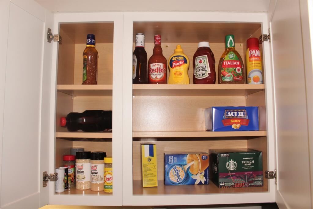 A kitchen cabinet with various condiments, spices, and coffee products.