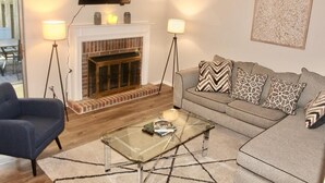 A living room with a sofa, armchair, glass coffee table, fireplace, and two floor lamps. - Cheerful 2 bedroom townhouse with indoor Fireplace (Tucker)