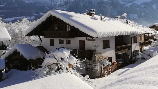 A chalet with a sloped roof covered in snow, surrounded by snow-covered trees and mountains in the background. - Königssee, vacation apartments Klausner (Schönau am Königssee)