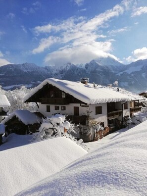 Un chalet doté d’un toit en pente recouvert de neige, entouré d’arbres et de montagnes enneigés.