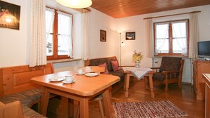 A cozy living room with a wooden ceiling, a dining table with chairs, a sofa, a TV, and a fireplace. - Königssee, vacation apartments Klausner (Schönau am Königssee)