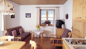 A cozy room with a wooden ceiling, a sofa, a dining table with chairs, a kitchen area with a sink, and a window with curtains. - Königssee, vacation apartments Klausner (Schönau am Königssee)