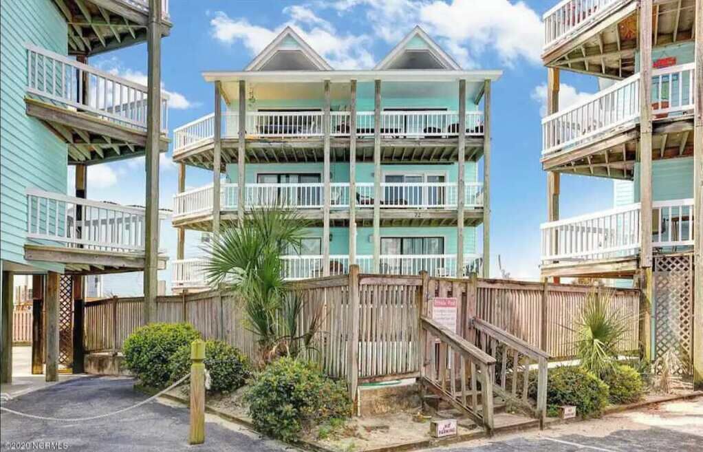 A beachfront hotel with multiple balconies, wooden railings, and a wooden fence.