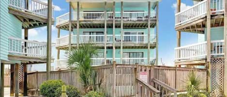 Un hôtel situé en bord de mer, doté de nombreux balcons, de rampes en bois et d’une clôture en bois.