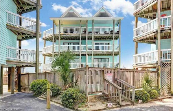 A beachfront hotel with multiple balconies, wooden railings, and a wooden fence.