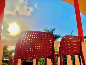 Deux chaises en plastique rouge, dont le dossier est ajouré, sont placées face à un ciel ensoleillé.