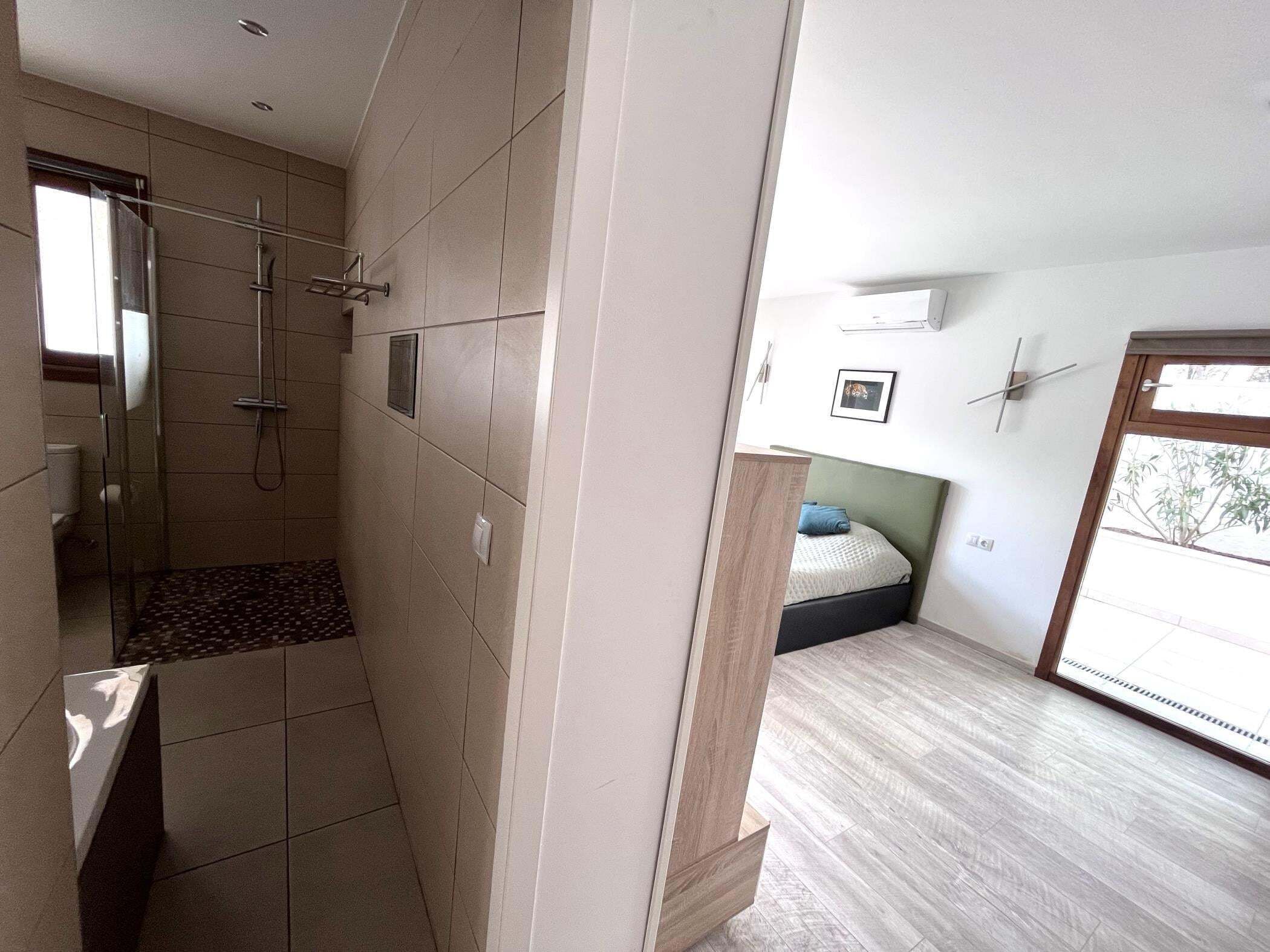 A modern bathroom with a shower, toilet, and a small window.