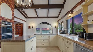 A kitchen with a brick oven, white cabinets, a large island, and a view of the outdoors through a window.