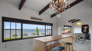A room with a large window overlooking a body of water, a wooden bar area, and a chandelier.
