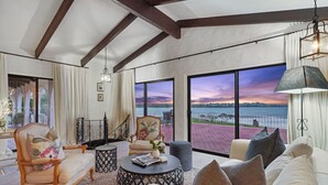A spacious living room with a large window offering a view of the water. There are multiple seating areas, including a sofa and a chair.