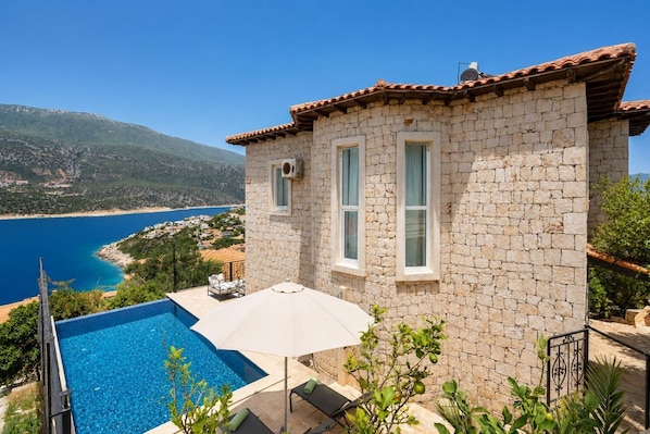 Ein Steinhaus mit Pool, einer Terrasse mit Tisch und Stühlen sowie Blick auf das Meer und die Berge.