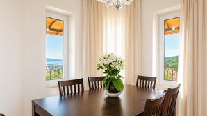 A dining room with a table, chairs, a vase with flowers, and windows with curtains.