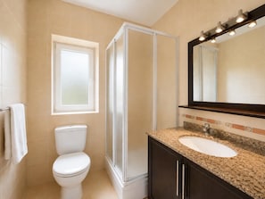 Ein Badezimmer mit Toilette, Duschkabine, Waschbecken mit Waschtisch und einem beleuchteten Spiegel.