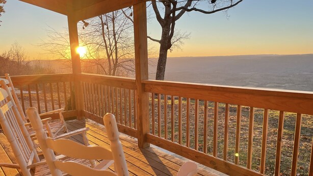Eine Holzterrasse mit weißen Stühlen und Geländer, mit Blick auf eine Landschaft bis zum Horizont.