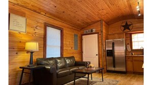 Ein gemütliches Blockhaus-Interieur mit Holzbalkendecke, einer schwarzen Ledersofa, einem kleinen Tisch, einem Kühlschrank und einer Küchenzeile.