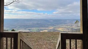 Blick von einer Holzdielen-Terrasse über ein Tal mit weitläufigen Feldern und einem bewölkten Himmel.
