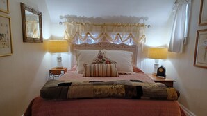 A bedroom with a bed, two bedside lamps, a clock, and a window with curtains.