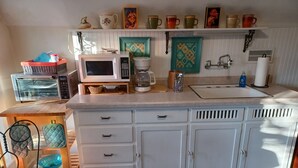 A kitchen with a microwave, toaster, coffee maker, and a sink. There are cabinets, a chair, and a rug.