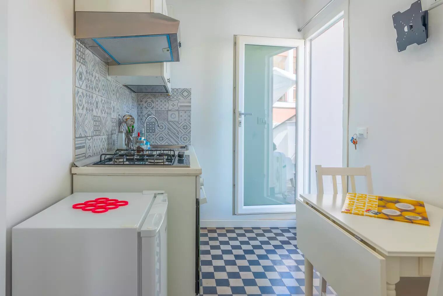 A compact kitchen with a gas stove, a refrigerator, and a checkered floor.