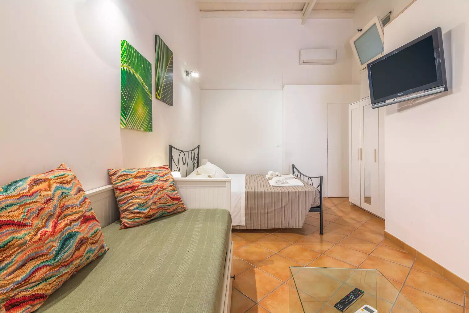Une petite pièce bien éclairée, comprenant un lit, une table de chevet, une chaise, un téléviseur fixé au mur et une armoire.