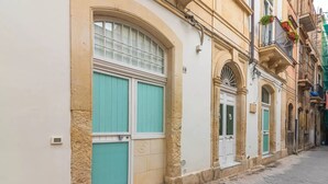 Una calle estrecha con edificios que tienen ventanas y puertas grandes, algunas con contraventanas.