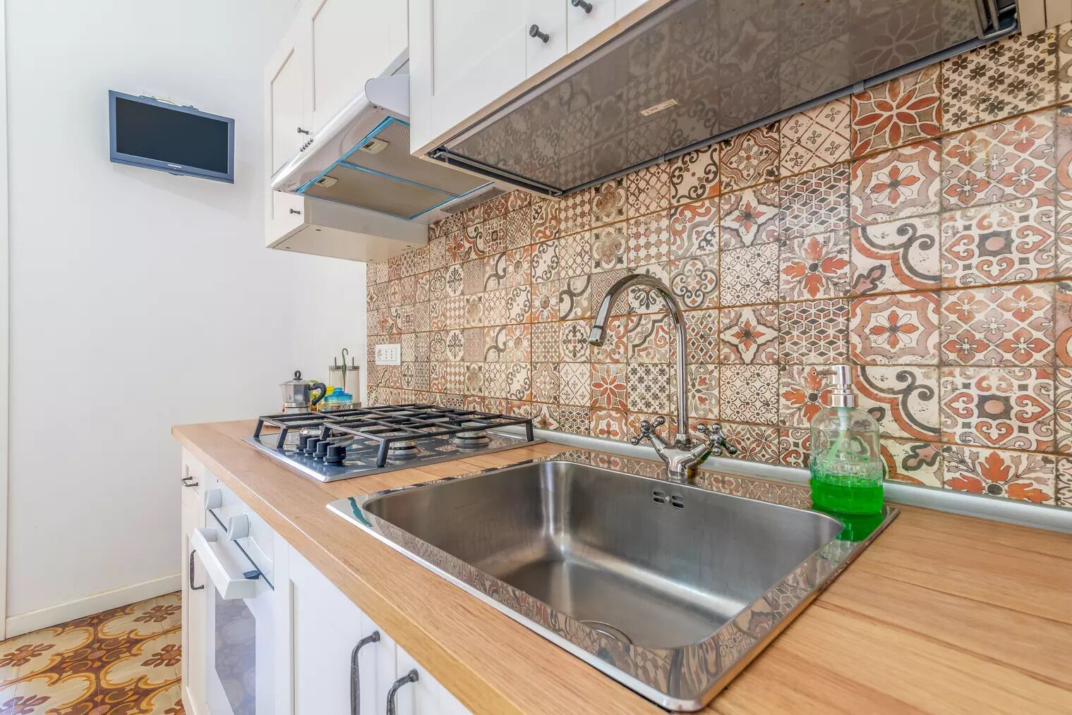 A kitchen with a gas stove, stainless steel sink, and decorative tile backsplash.