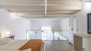 Un dormitorio moderno con una cama grande, techo de madera y vistas a una escalera que lleva a un balcón.