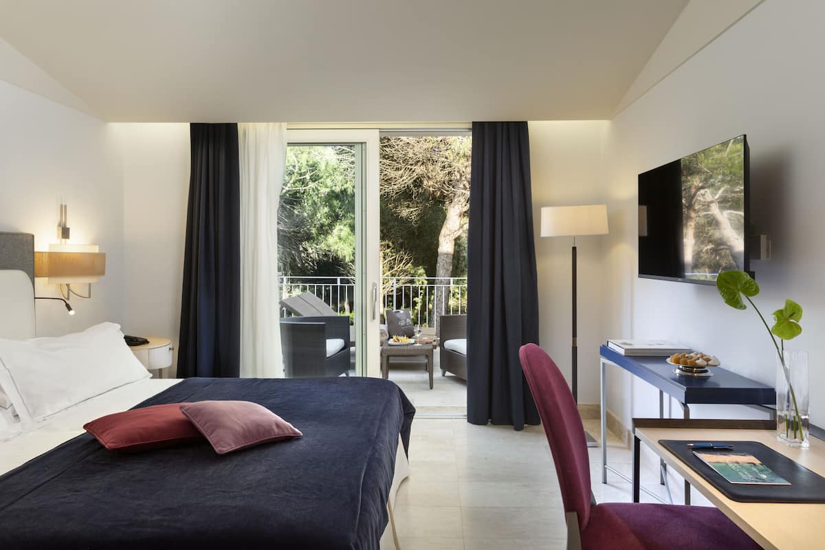 Une chambre d’hôtel comprenant un lit, un bureau, une chaise, une télévision et un balcon aménagé avec du mobilier d’extérieur.