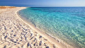 Una playa arenosa con agua turquesa cristalina y cielo despejado.