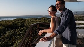 Una pareja en un balcón con vistas a un paisaje costero que incluye el océano y colinas al lejano.