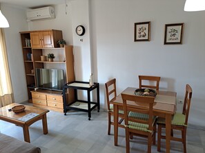 A living room with a TV, wooden furniture, a dining table with chairs, and wall-mounted decorations.