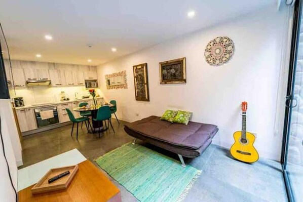 A compact living space with a kitchenette, a dining area, and a sofa with a guitar.