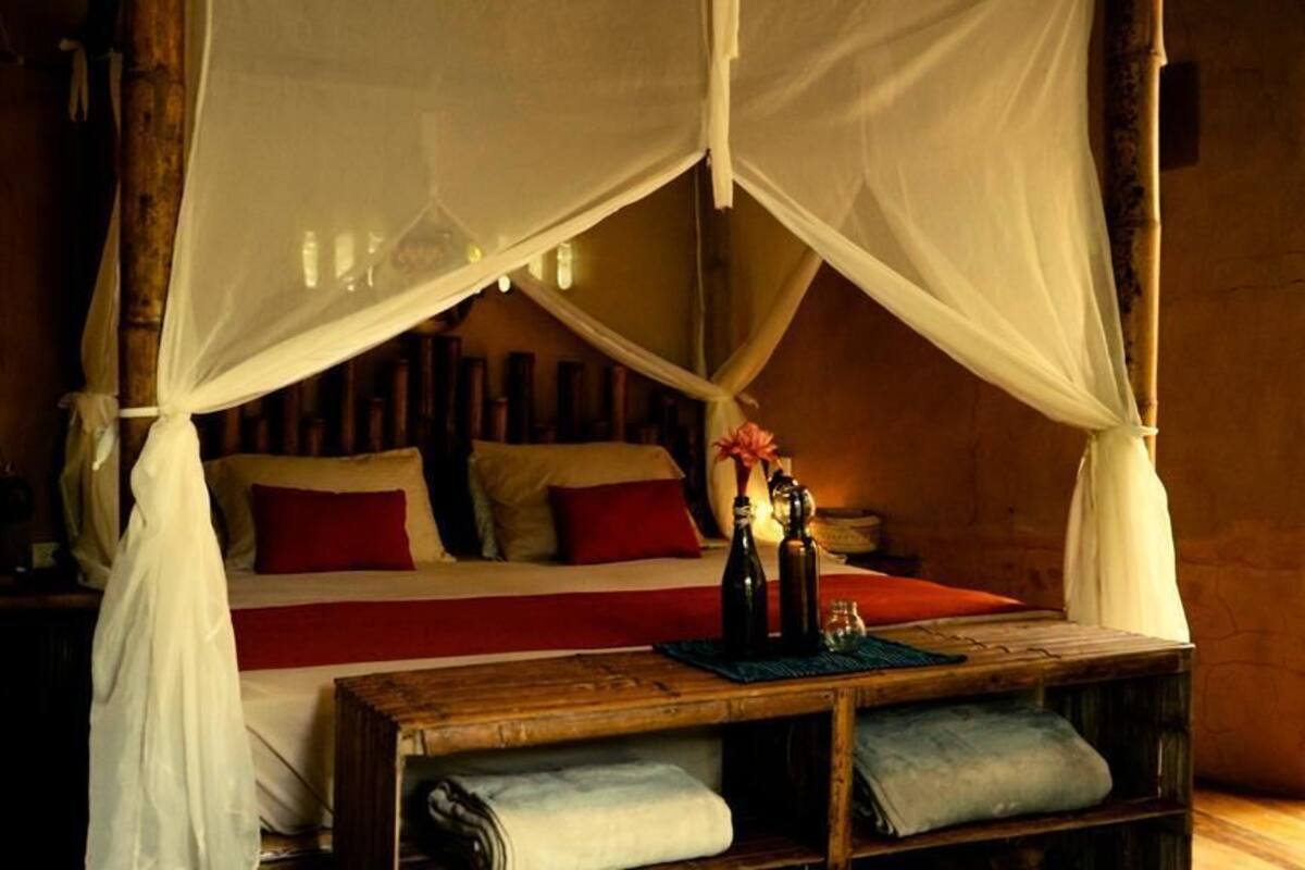 A bed with a canopy, pillows, a bedside table with a bottle and glasses, and a nightstand.