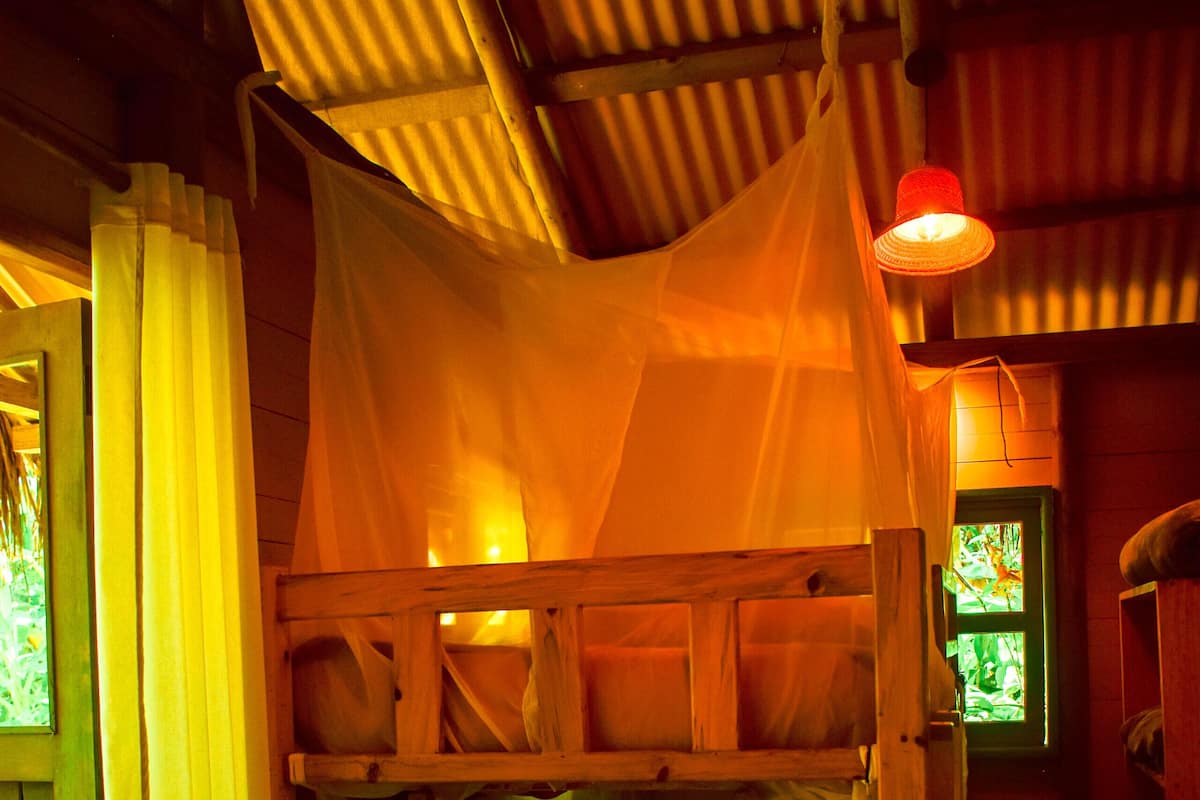 A bunk bed with a mosquito net, wooden headboard, and a small window with a view.