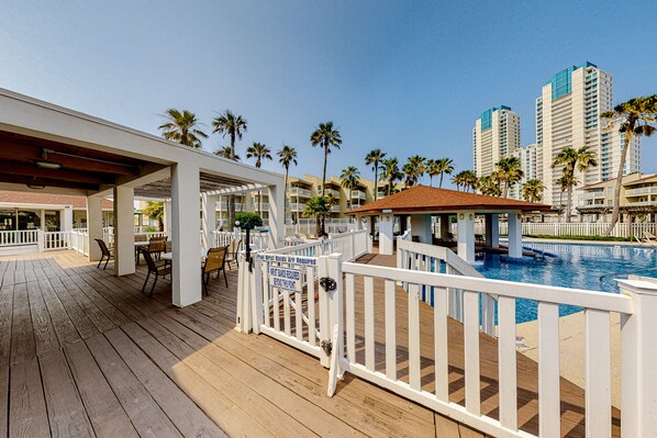 A wooden deck with outdoor seating, a pool, and high-rise buildings in the background.