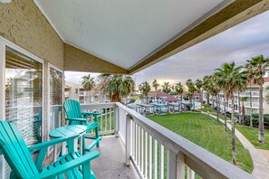 A balcony with turquoise chairs and a view of a well-maintained lawn and buildings in the background.
