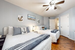 A bedroom with two beds, a ceiling fan, artwork on the walls, and a wooden floor.