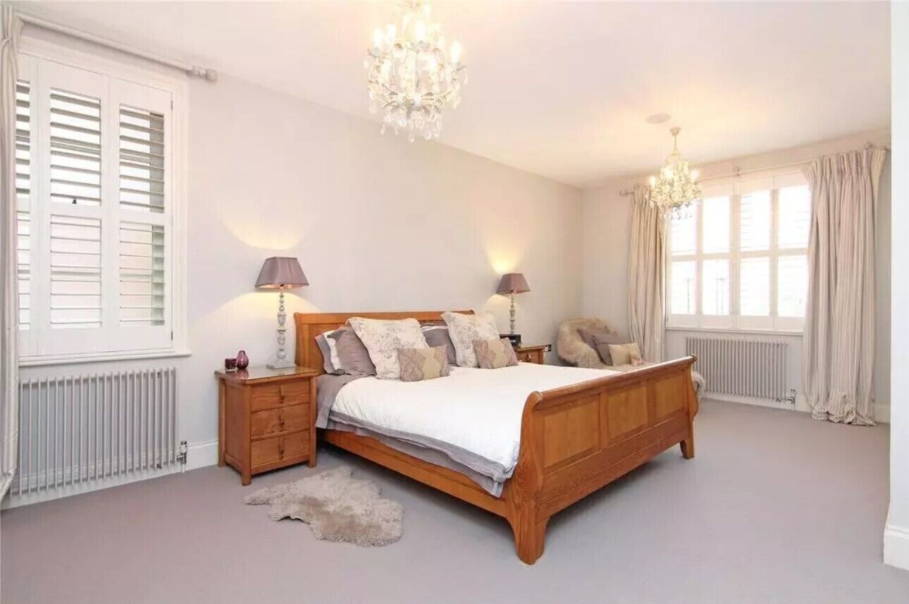 Ein Schlafzimmer mit einem hölzernen Bett, zwei Nachttischen, einer Chandelüster und einem Fenster mit Vorhängen.