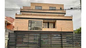 A modern two-story house with a brick facade, large windows, and a black metal fence. - Beautiful Suite in Cuenca (Cuenca)