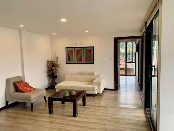 A spacious living room with a sofa, a coffee table, and a painting on the wall. - Beautiful Suite in Cuenca (Cuenca)