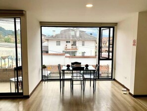 A spacious room with a large sliding glass door leading to a balcony, a dining table with chairs, and a view of a residential area. - Beautiful Suite in Cuenca (Cuenca)