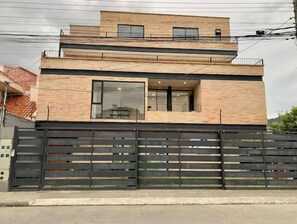 A modern two-story house with a brick facade, large windows, and a black metal fence.