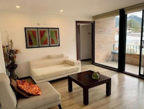 A living room with a sofa, a coffee table, and a large sliding glass door leading to a balcony. - Beautiful Suite in Cuenca (Cuenca)