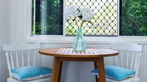 A white wooden chair with a blue cushion, a round wooden table, and a vase with white flowers. - Seascape Whitsundays (Airlie Beach)