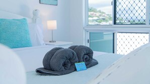 A neatly made bed with two rolled towels and a thank you card. - Seascape Whitsundays (Airlie Beach)