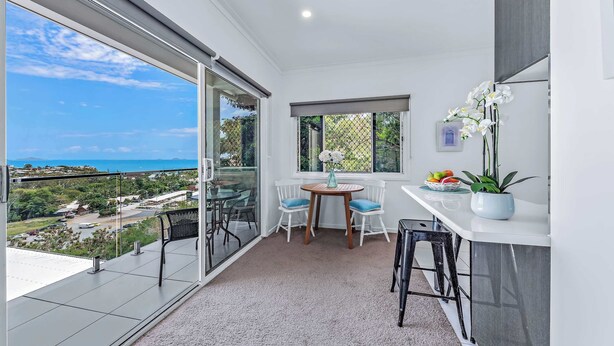 A balcony with a view of the sea, a small table with chairs, and a potted plant. - Seascape Whitsundays (Airlie Beach)
