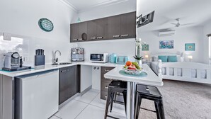 A modern kitchen with a central island, built-in appliances, and a dining area with a white table and bar stools. - Seascape Whitsundays (Airlie Beach)