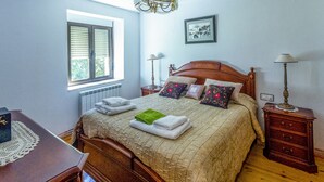 A bedroom with a wooden bed, a window with blinds, a radiator, a bedside table with a lamp, and a picture on the wall. - enjoy the nature (NOCEDO DE CURUEÑO)