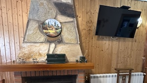 A fireplace with a stone mantle, a TV mounted on the wall, and a wicker basket on the floor. - enjoy the nature (NOCEDO DE CURUEÑO)