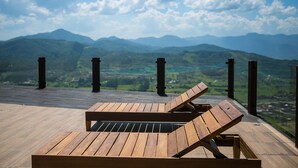 A wooden deck with two lounge chairs overlooking a mountainous landscape.